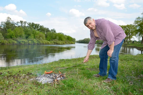 L'uomo in fiamme vicino al fiume frigge salsicce . — Foto Stock