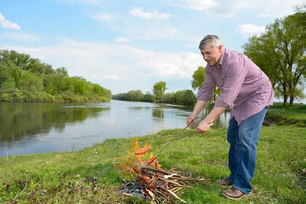 Hombre en llamas cerca del río freír salchichas . — Foto de Stock