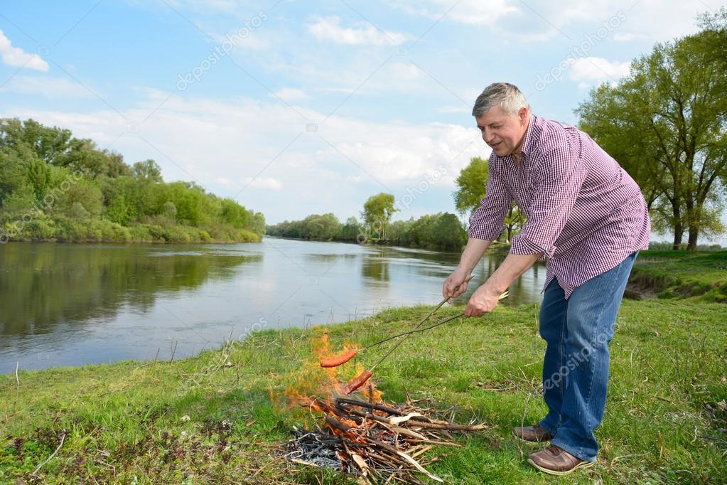 Man on fire near the river fry sausages.