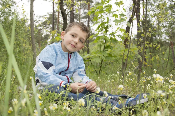 Der Junge im Wald, der neben den Blumen sitzt. — Stockfoto