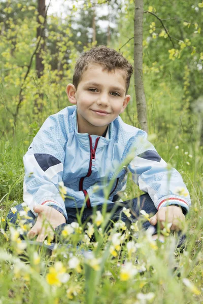 Der Junge im Wald, der neben den Blumen sitzt. — Stockfoto