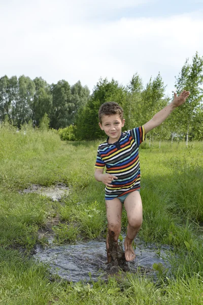 Boso chłopiec biegnie przez kałużę. — Zdjęcie stockowe