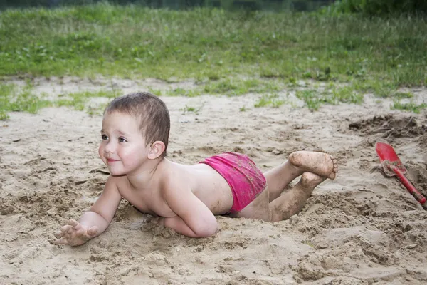 Funny holčička ležela na písku poblíž jezera v létě a — Stock fotografie