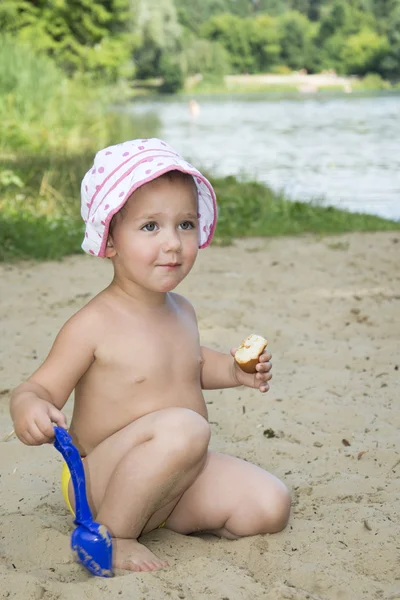 Niña divertida se sienta en la arena cerca del lago en verano y s — Foto de Stock