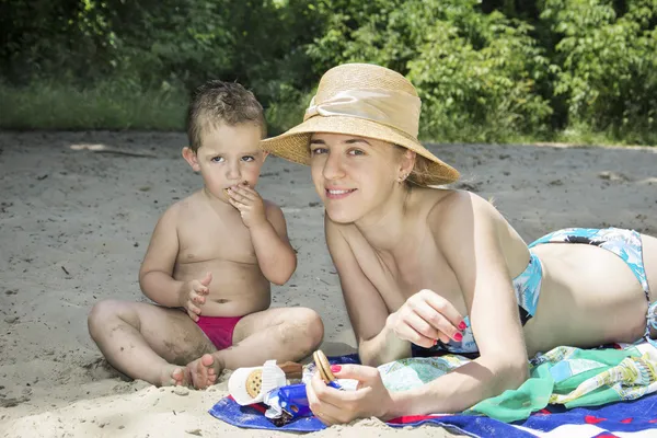 Verão na praia mãe com uma criança comer biscoitos . — Fotografia de Stock