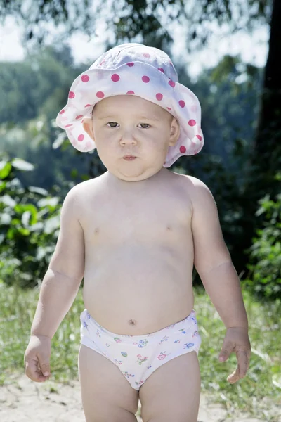 Little girl in a pants standing on the beach near the bushes. — Stock Photo, Image