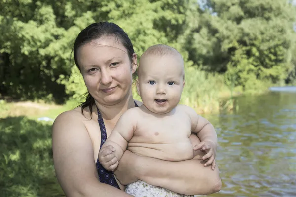 Літній час на пляжі біля річки мама тримає в руках маленького сина — стокове фото