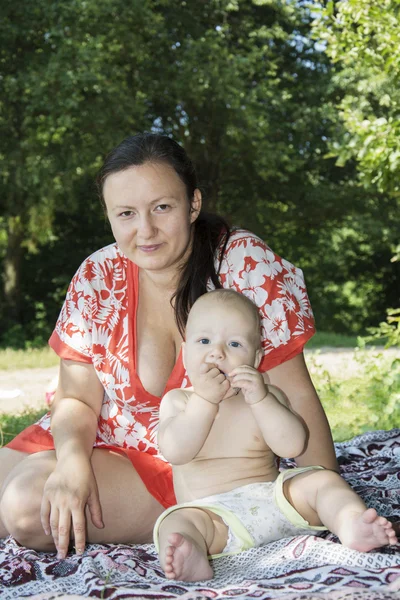 Mamá y su hijo pequeño sentado en una toalla en la playa cerca del arbusto —  Fotos de Stock
