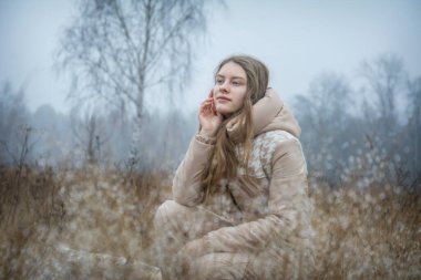 Sonbaharda soğuk, soğuk bir sabah tarlada, uzun saçlı bir kız çiğ damlalarıyla çimlerde.