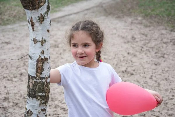 彼女の手にピンクの風船と小さな美しい女の子が立っている白樺の近くの森の春には — ストック写真