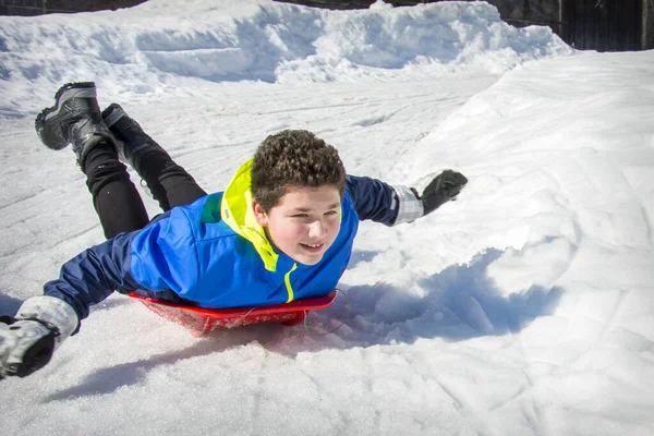 冬の晴れた日には 男の子が胃のプラスチック製のそりで丘を滑り降りる 彼は喜んでいる — ストック写真