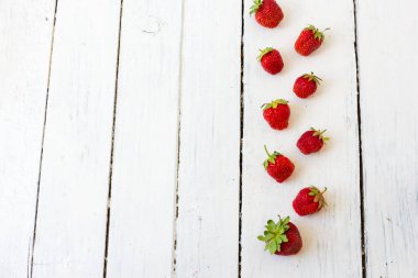 Olgun kırmızı çilek, ahşap beyaz arka plandaki çerçeve gibi bir desen içinde yatar. Uzayı kopyala Yukarıdan görüntüle