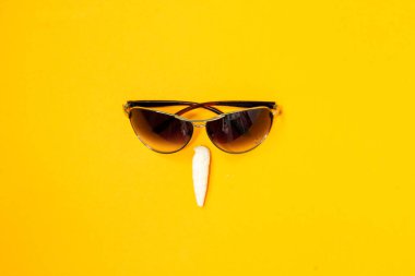 Güneş gözlüğü ve parlak sarı bir arka planda deniz kabuğu. Yaratıcı yüz. seçici odak, kopyalama alanı, pankart.