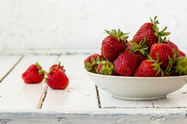 Olgun kırmızı çilekler, beyaz bir fincanda, tahta beyaz bir masada yatıyor. Boşluğu kopyala.