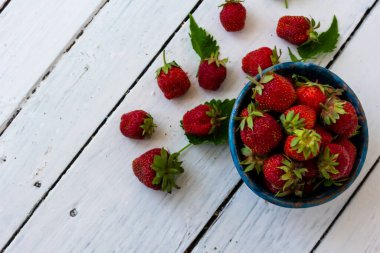 Olgun kırmızı çilekler ahşap beyaz bir masada mavi bir fincanda yatar. Tatlı böğürtlenler yakınlarda. Uzayı kopyala Fotoğrafın üst görünümü.
