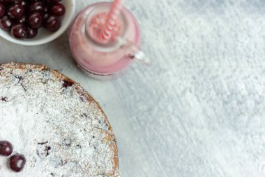 Ev yapımı vişneli turta ve kırmızı vişneli smoothie ve gri bir masaya serpiştirilmiş çilek, yakın plan. Yaz kahvaltısı.