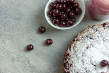 Ev yapımı vişneli turta ve kırmızı vişneli smoothie ve gri bir masaya serpiştirilmiş çilek, yakın plan. Yaz kahvaltısı.