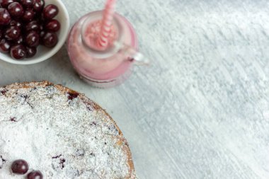 Ev yapımı vişneli turta ve kırmızı vişneli smoothie ve gri bir masaya serpiştirilmiş çilek, yakın plan. Yaz kahvaltısı.