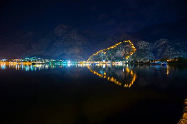 Kentin Kotor kentinin ışıkları ve bir su üzerindeki yansıma, akşam boyunca kalplerin gölgesini siliyor, Karadağ.
