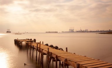 An old long pier and an old rowboat by the sea, photographed with long exposure technique.