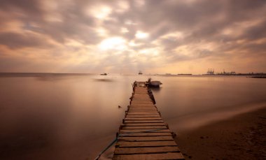 An old long pier and an old rowboat by the sea, photographed with long exposure technique.