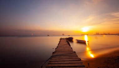 An old long pier and an old rowboat by the sea, photographed with long exposure technique.