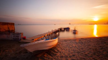 An old long pier and an old rowboat by the sea, photographed with long exposure technique.
