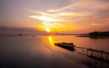An old long pier and an old rowboat by the sea, photographed with long exposure technique.