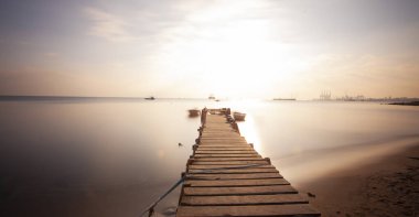 An old long pier and an old rowboat by the sea, photographed with long exposure technique.