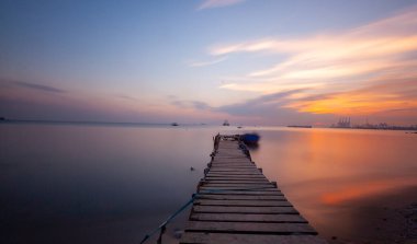An old long pier and an old rowboat by the sea, photographed with long exposure technique.