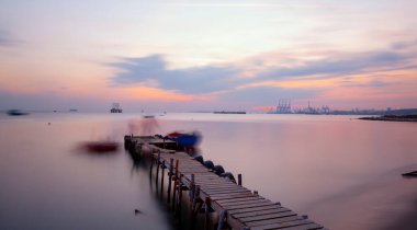An old long pier and an old rowboat by the sea, photographed with long exposure technique.