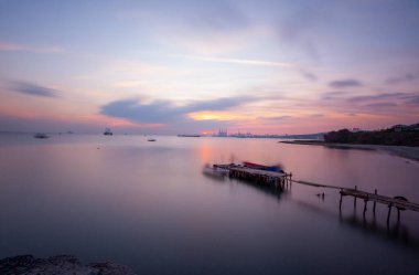 An old long pier and an old rowboat by the sea, photographed with long exposure technique.
