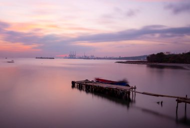 An old long pier and an old rowboat by the sea, photographed with long exposure technique.