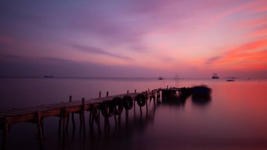 An old long pier and an old rowboat by the sea, photographed with long exposure technique.
