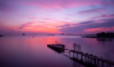 An old long pier and an old rowboat by the sea, photographed with long exposure technique.