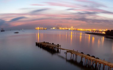 An old long pier and an old rowboat by the sea, photographed with long exposure technique.