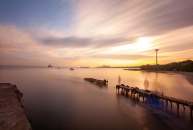 An old long pier and an old rowboat by the sea, photographed with long exposure technique.