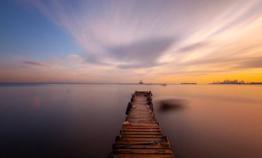 An old long pier and an old rowboat by the sea, photographed with long exposure technique.