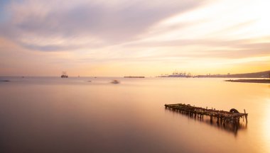 An old long pier and an old rowboat by the sea, photographed with long exposure technique.