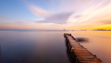 An old long pier and an old rowboat by the sea, photographed with long exposure technique.