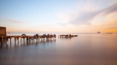 An old long pier and an old rowboat by the sea, photographed with long exposure technique.