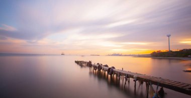 An old long pier and an old rowboat by the sea, photographed with long exposure technique.