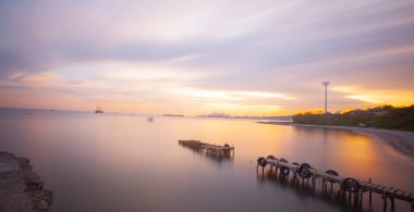 An old long pier and an old rowboat by the sea, photographed with long exposure technique.