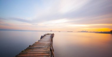 An old long pier and an old rowboat by the sea, photographed with long exposure technique.