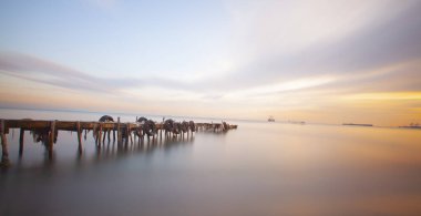 An old long pier and an old rowboat by the sea, photographed with long exposure technique.