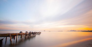 An old long pier and an old rowboat by the sea, photographed with long exposure technique.