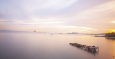 An old long pier and an old rowboat by the sea, photographed with long exposure technique.