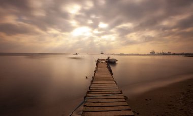 An old long pier and an old rowboat by the sea, photographed with long exposure technique.
