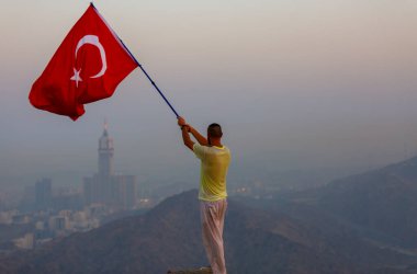 Türkçe bayrak sallıyor, zam kulesi arkada.