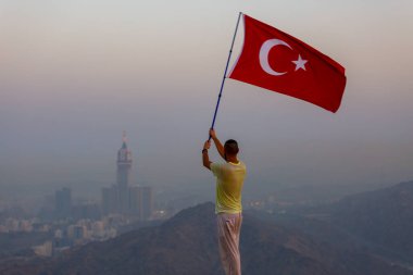 Türkçe bayrak sallıyor, zam kulesi arkada.
